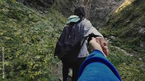 First person view of a young woman with a backpack leads by the hand during a walk together on the mountain trail between dense grass. Concept of active outdoor hike tourism