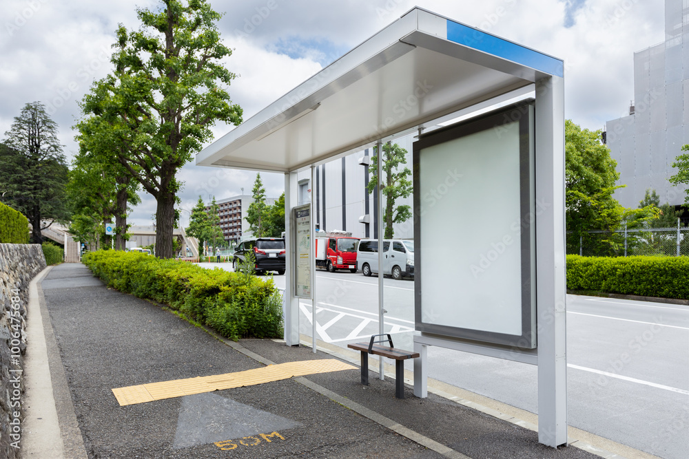 A vertical blank billboard at a bus stop shelter on a street in Tokyo, near by a park. Copy space screen on a lightbox for displaying advertising messages and promotional content
