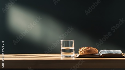 A glass of water and a small loaf of bread rest beside an open Bible on a wooden table, surrounded by soft, dark lighting that invites spiritual contemplation and fasting photo