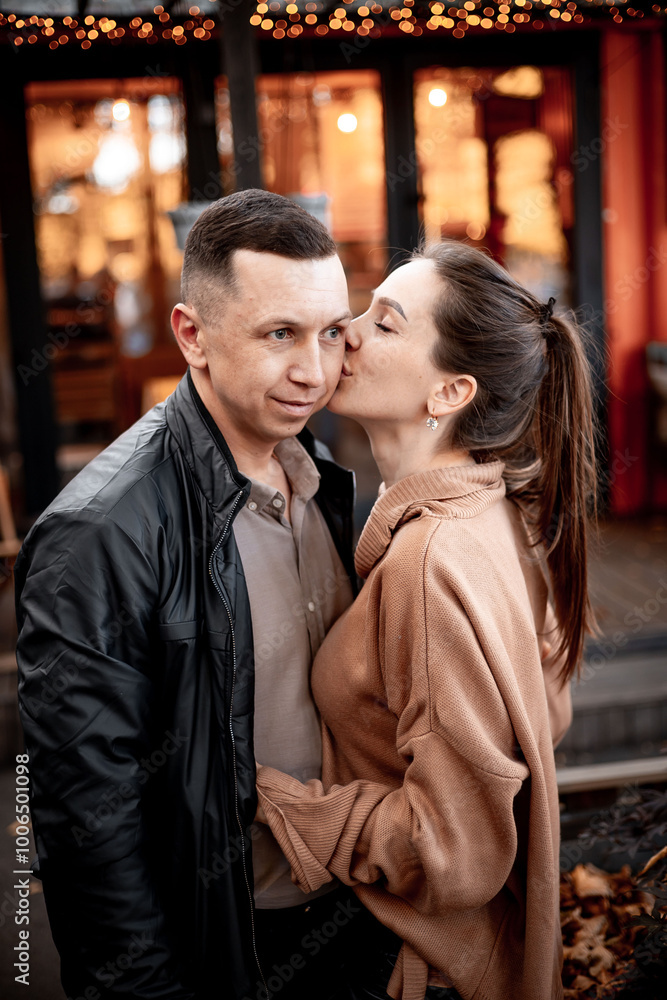 Fototapeta premium a young couple guy with a girl in autumn in a cafe in brown and orange tones on an outdoor terrace hugging and kissing, love or Valentine's day
