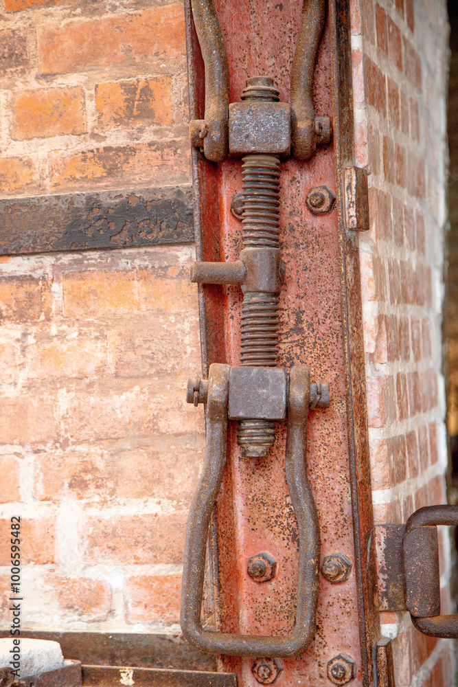 Close-up of a rusted screw and clamp mechanism, highlighting the aged metal's corrosion. The industrial part contrasts with the blurred background of brick and worn surroundings. Close-up of a rusted screw and clamp mechanism, highlighting the aged metal's corrosion. The industrial part contrasts with the blurred background of brick and worn surroundings.