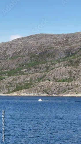 Kviby, Alta Municipality, Finnmark, Norway - small white vessel slowly cruising parallel to the coastline bays at a sunny day while leaving the fjord photo