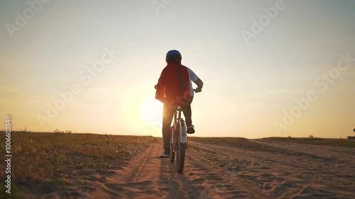 Child superhero cape rides bicycle at sunset feeling freedom and adventure. child pedals bicycle embracing superhero role. Imaginative play brings freedom as child dreams heroic adventures on bicycle.