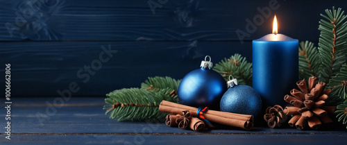 Blue christmas candle burning with ornaments and pine sprigs on a rustic blue wooden background