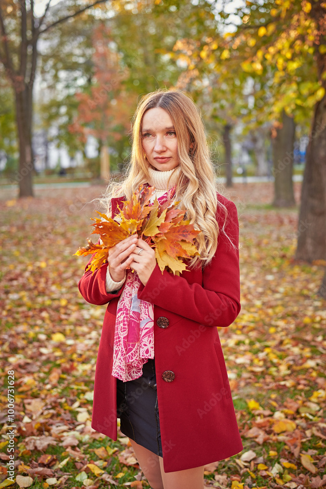 A woman in a red coat and a black skirt walks in an autumn park. The concept of autumn and the beauty of nature. A woman in a red coat and a black skirt walks in an autumn park. The concept of autumn and the beauty of nature.