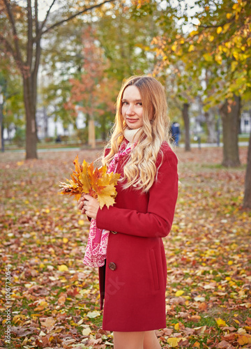 A woman in a red coat and a black skirt walks in an autumn park. The concept of autumn and the beauty of nature.