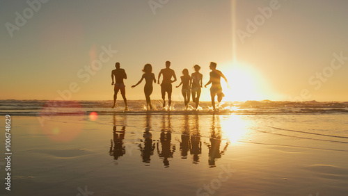 Group Of Friends In Swimwear Run Out Of Waves At Sunset On Summer Beach Vacation 