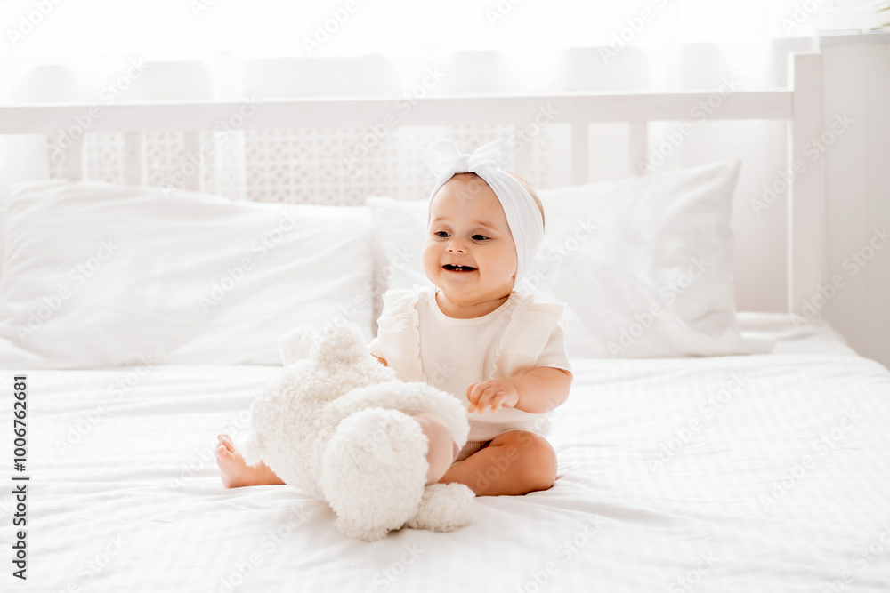 smiling baby girl sitting on the bed in white clothes in a brigh smiling baby girl sitting on the bed in white clothes in a brigh
