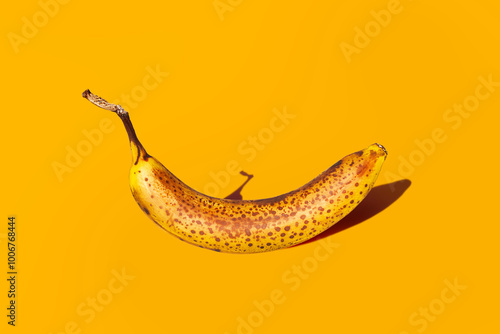 Fotografija Ripe or overripe banana with dark spots with deep shadow isolated on bright orange background closeup, in front