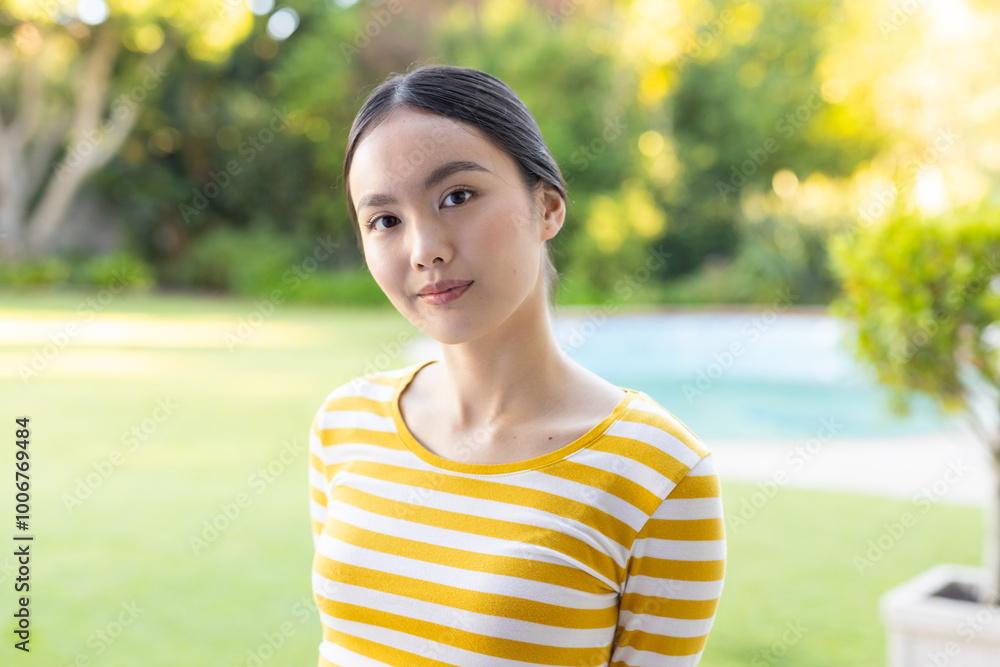 Smiling young asian woman in yellow striped shirt standing outdoors in garden setting Smiling young asian woman in yellow striped shirt standing outdoors in garden setting