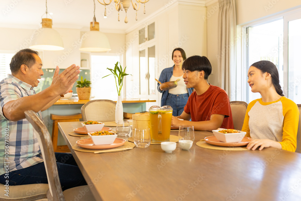 Multiracial family enjoying meal together, smiling and talking at dining table in kitchen Multiracial family enjoying meal together, smiling and talking at dining table in kitchen