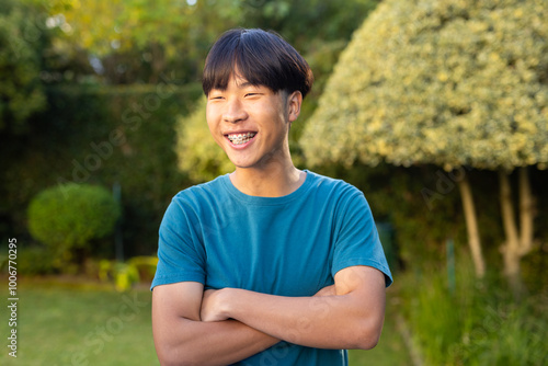 Smiling asian teenage boy with braces standing outdoors, crossing arms in garden