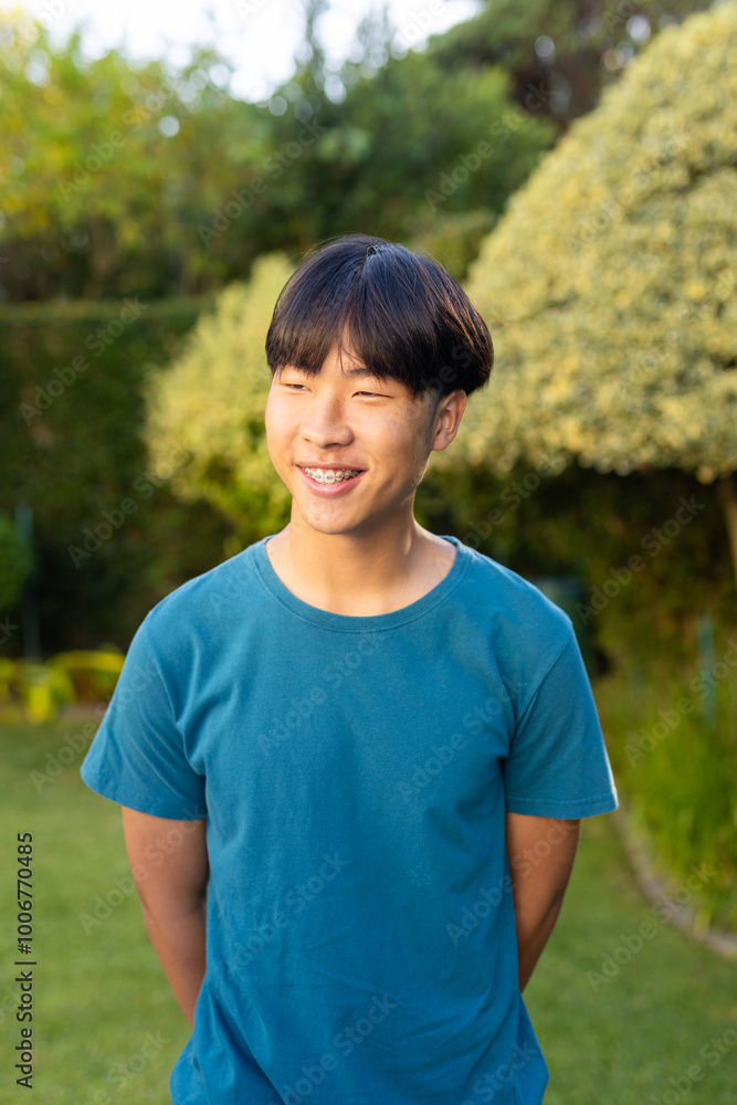 Smiling young asian teenage boy in blue shirt standing in garden, enjoying outdoor time Smiling young asian teenage boy in blue shirt standing in garden, enjoying outdoor time