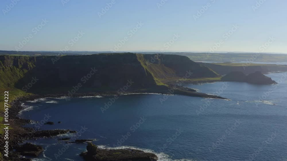 Aerial pan over the Amphitheatre and Giant's Causeway, showcasing a stunning coastal view under a sunny evening sky. Aerial pan over the Amphitheatre and Giant's Causeway, showcasing a stunning coastal view under a sunny evening sky.