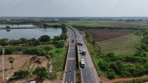 A cinematic aerial shot captures the less traffic on the pristine Chennai-Vijayawada highway, with towering high-voltage power lines casting long, dramatic shadows across the gleaming black asphalt. photo