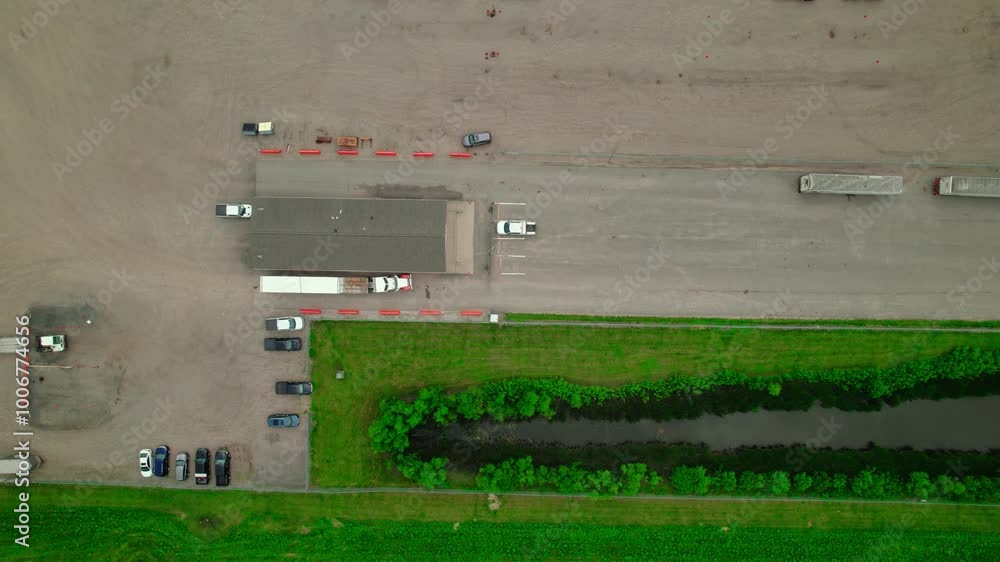 Top-down aerial view of flatbed semi-trucks at the check-in guard station of an industrial plant. Top-down aerial view of flatbed semi-trucks at the check-in guard station of an industrial plant.