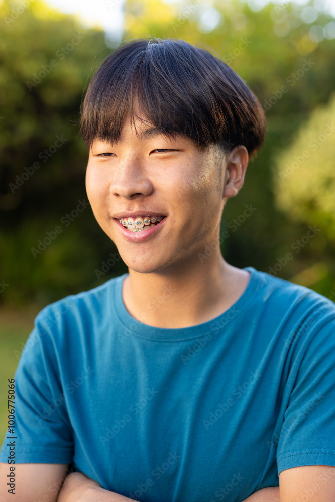 Smiling asian teenage boy with braces wearing blue shirt outdoors in garden