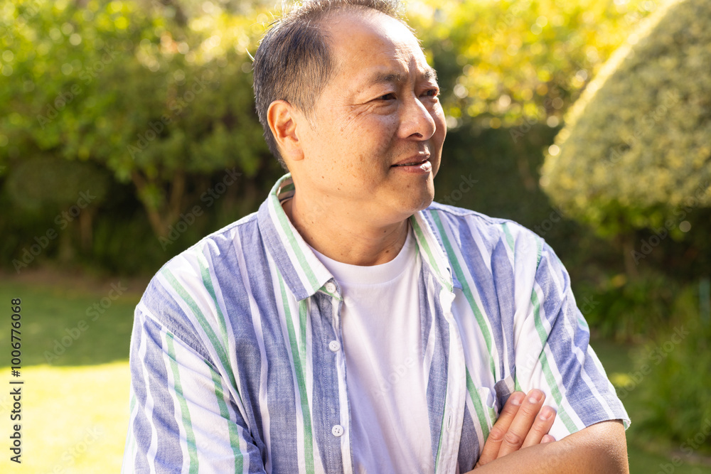 Smiling asian middle-aged man in casual shirt standing outdoors in garden, enjoying sunny day Smiling asian middle-aged man in casual shirt standing outdoors in garden, enjoying sunny day