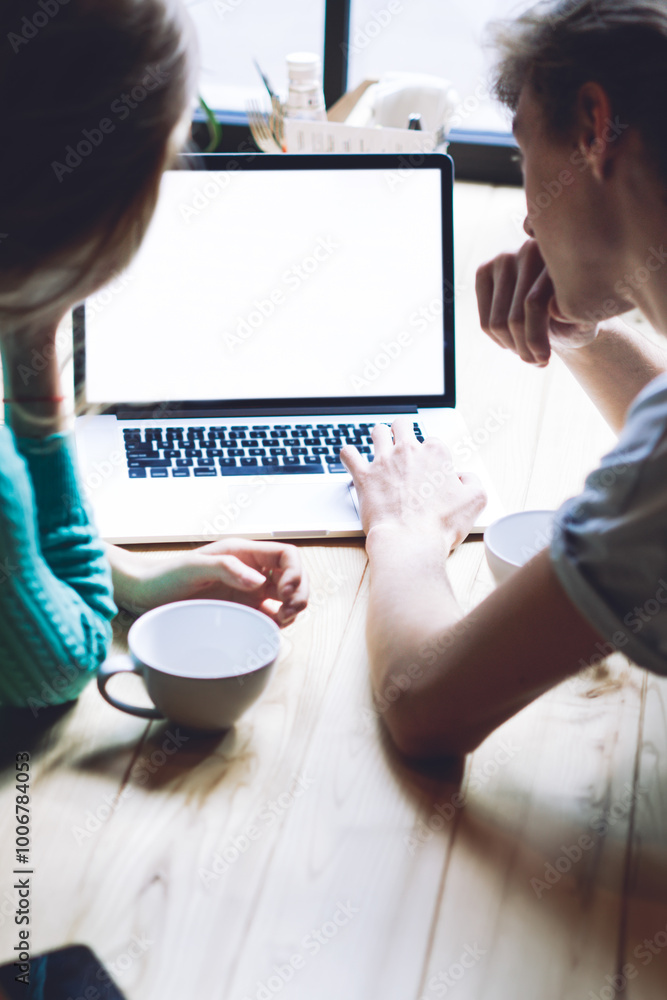 Fototapeta premium Back view of romantic couple searching information about good hotels for making booking online on travel web page, skilled male and female installing application for blogging on modern netbook