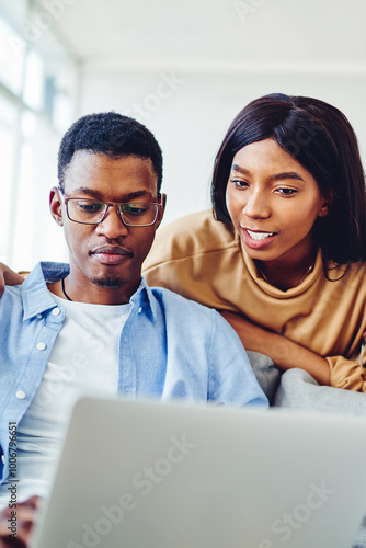 Young African American couple in love making shopping on web page via laptop computer staying at home, smiling dark skinned hipster guys watching video on netbook resting on free time in apartment