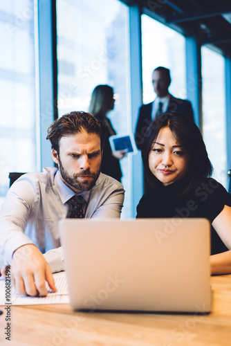 Concentrated diverse male and female office workers analyzing information on financial website on laptop during brainstorming, concept of teamwork and collaboration. Two colleagues cooperating in team