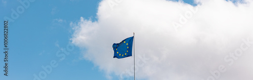 European Union flag on the roof top of a buildng in center of a city.  Windy day in the summer, blue sky with clouds in the background.