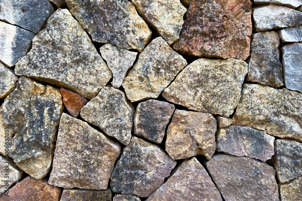 Fototapeta premium Rough grainy surface of wall stones. Background texture with brown and blue hues outdoors