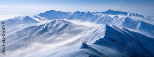 A snow-covered mountain range under a clear blue sky, with white clouds swirling around the peaks.