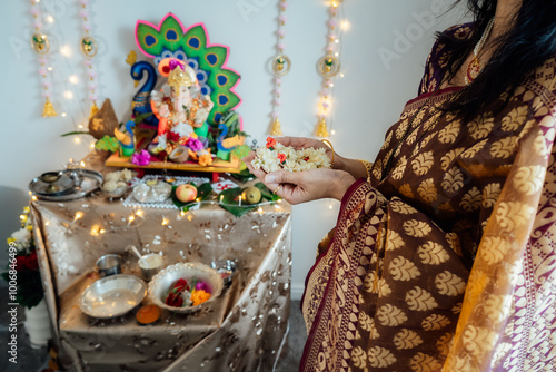 Indian woman dressed in traditional wear engages in worship at home altar, adorned with decors and offerings for god Ganesha during festive celebration. Indian culture, hindu ritual and customs. photo