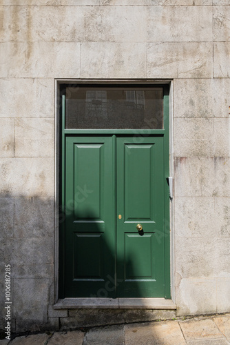 Classic green wooden door with brass handle on stone facade in the sunshine