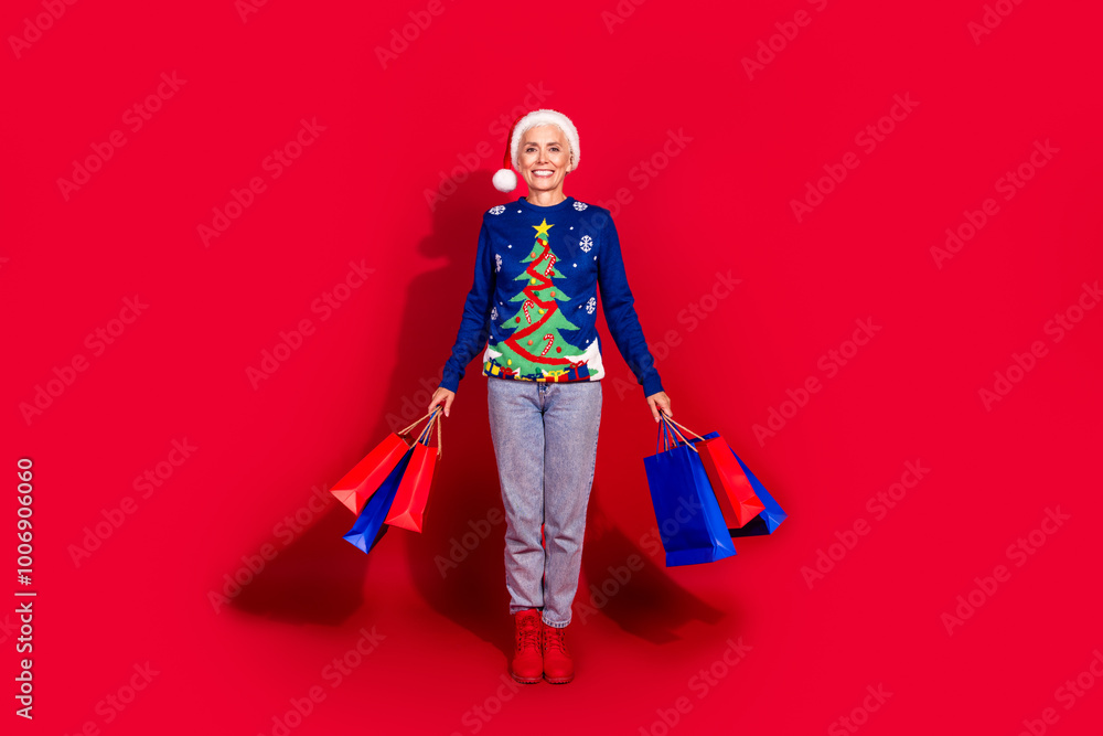 Full body portrait of pretty aged lady hold shop bags new year xmas isolated on vibrant red color background Full body portrait of pretty aged lady hold shop bags new year xmas isolated on vibrant red color background