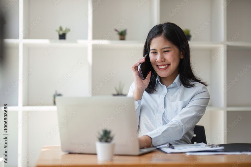 Professional Business Woman Talking on Phone While Working on Laptop in Modern Office Setting Professional Business Woman Talking on Phone While Working on Laptop in Modern Office Setting