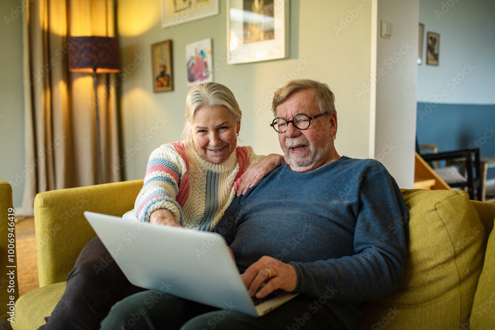 Happy senior couple sitting on couch using laptop together Happy senior couple sitting on couch using laptop together