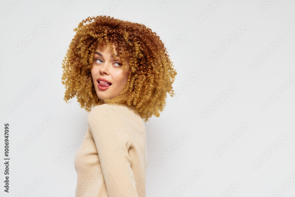 Curly haired woman with a playful expression against a plain background, showcasing a light sweater and vibrant hairstyle, emphasizing confidence and self expression Curly haired woman with a playful expression against a plain background, showcasing a light sweater and vibrant hairstyle, emphasizing confidence and self expression