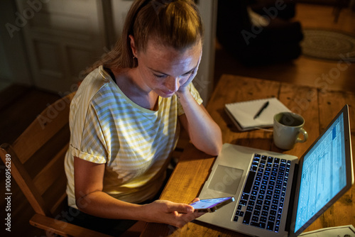 Woman late night working on laptop and smartphone at home photo