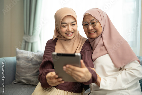Two muslim mother and daughter using tablet in a living room at home