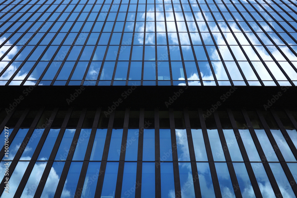 Fragment of office building facade made of blue toned glass and steel constructions under blue sky. Perspective view from below to modern skyscraper. Background image with place for text.