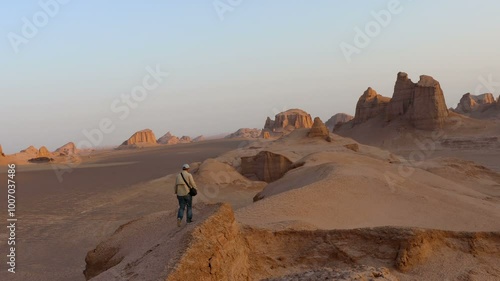 A lone man watches from a hilltop at sunrise among the Kaluts in the Lut Desert Iran