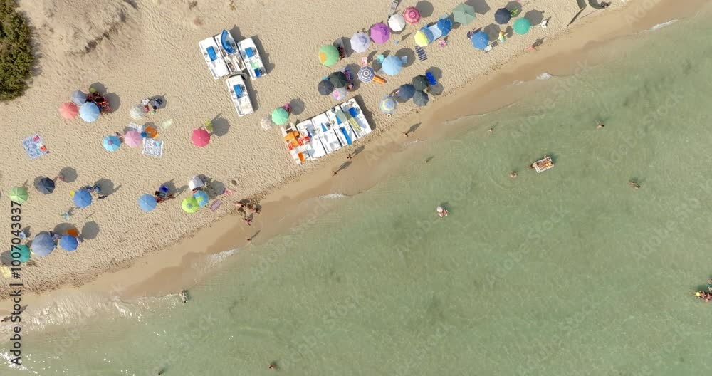 Aerial perpendicular view of people vacationing on the beach of San Pietro in Bevagna, in Salento, Puglia, Italy. There are many beach umbrellas on the shore of that public beach. Holidays concept. Aerial perpendicular view of people vacationing on the beach of San Pietro in Bevagna, in Salento, Puglia, Italy. There are many beach umbrellas on the shore of that public beach. Holidays concept.