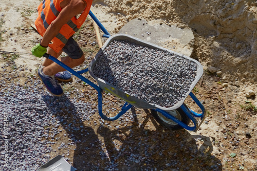 A worker is driving a wheelbarrow filled with gravel at a construction site, working with gravel at a construction site, loading and delivery of gravel.