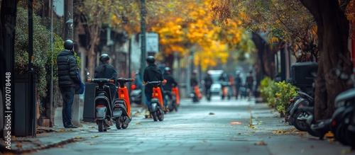 A row of parked scooters on a city street with a man standing in the foreground. The street is lined with trees, some of which have yellow leaves.