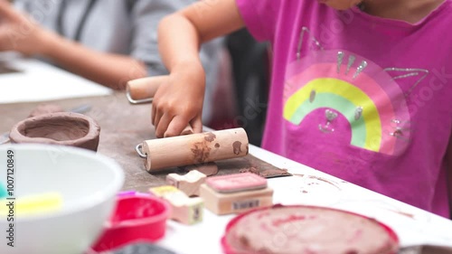 Young girl uses a rolling pin to flatten clay during an art class, Her engagement in the creative process highlights the joy and concentration involved in hands-on learning activities.