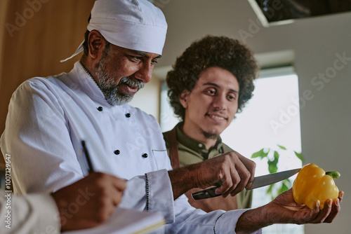 Fotografie Low angle shot of Indian professional chef showing peeling skills to his intern