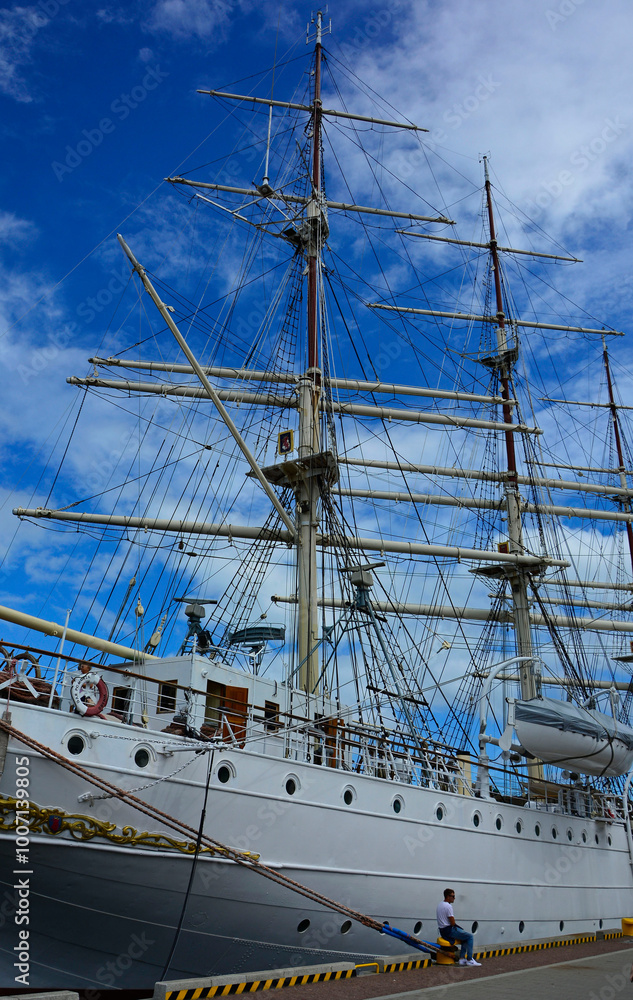 żaglowiec z masztami i olinowaniem, żaglowiec w porcie na tle niebieskiego nieba, Ship Mast and Ropes, ship moored in harbor of coastal town, sailing ship with rigging, Sailing ships moored in harbor