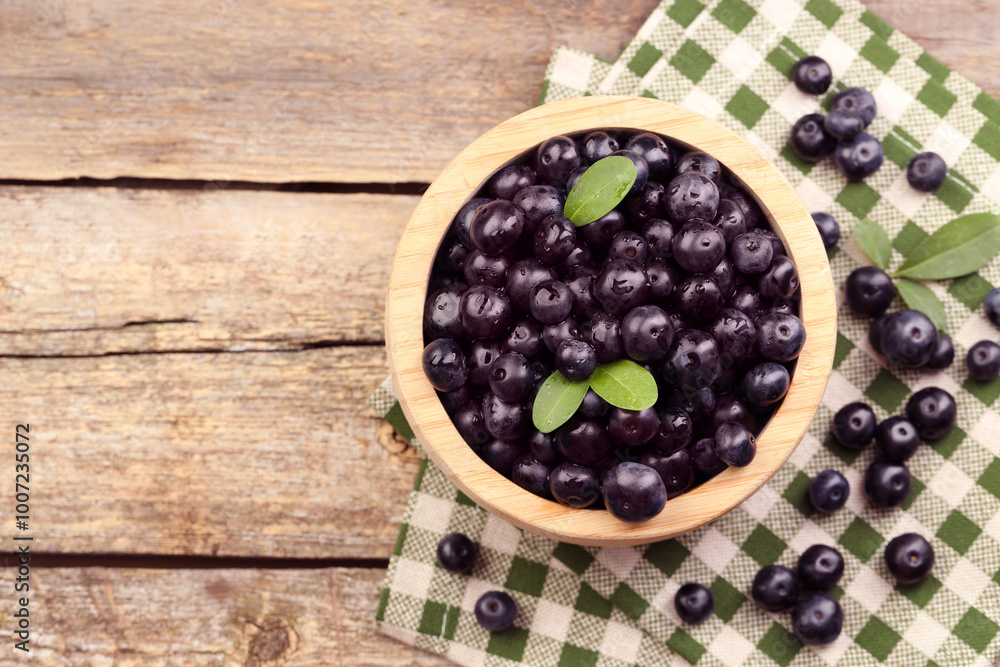 Ripe acai berries and leaves in bowl on wooden table, top view. Space for text Ripe acai berries and leaves in bowl on wooden table, top view. Space for text
