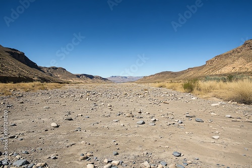 A stunning panoramic view of a dry riverbed in a desert landscape, surrounded by rocky hills under a clear blue sky.