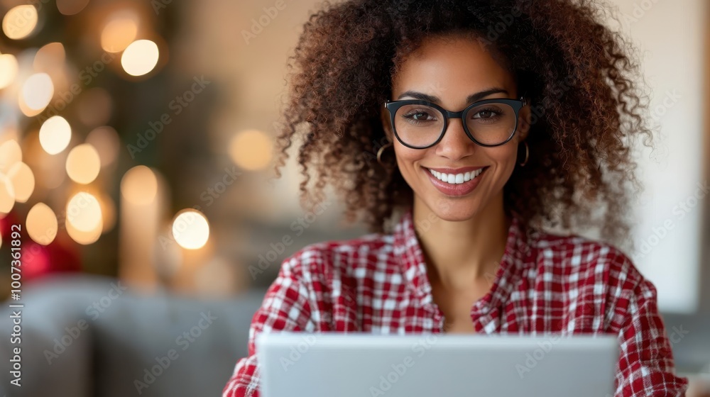 A woman with eyeglasses smiles while working on her laptop, surrounded by enchanting Christmas lights, creating a warm and pleasant festive atmosphere. A woman with eyeglasses smiles while working on her laptop, surrounded by enchanting Christmas lights, creating a warm and pleasant festive atmosphere.