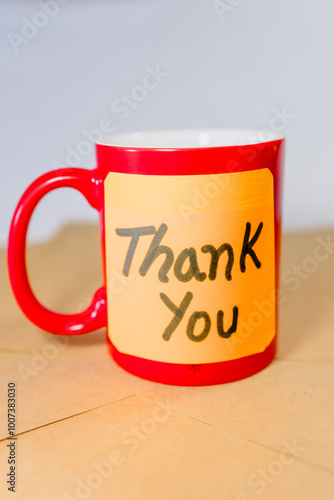 Thank you phrase written on a recycled cardboard with a red cup of coffee on the background of a notebook