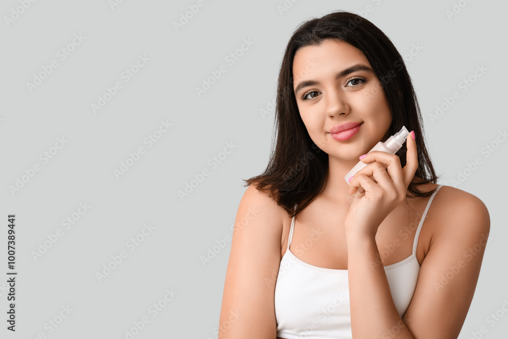 Fototapeta premium Beautiful young woman holding bottle of cosmetic product on grey background