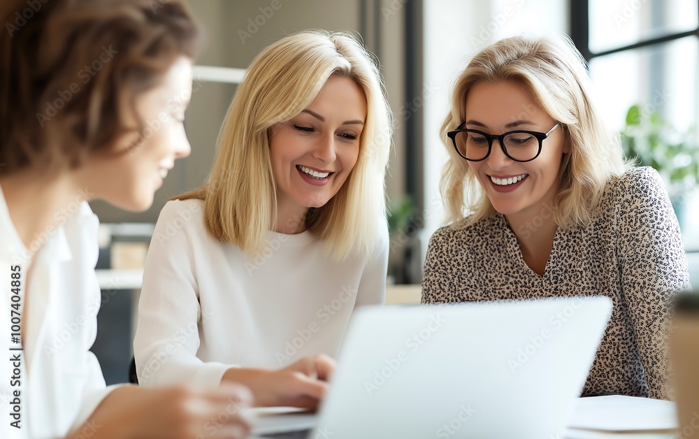 Three women sharing a joyful moment while collaborating on a laptop in a modern office setting, showcasing teamwork and creativity. Three women sharing a joyful moment while collaborating on a laptop in a modern office setting, showcasing teamwork and creativity.